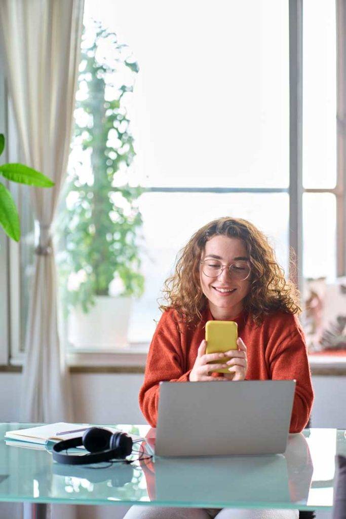 Young Smiling Woman Holding Smartphone Mobile Cell Phone At Home.