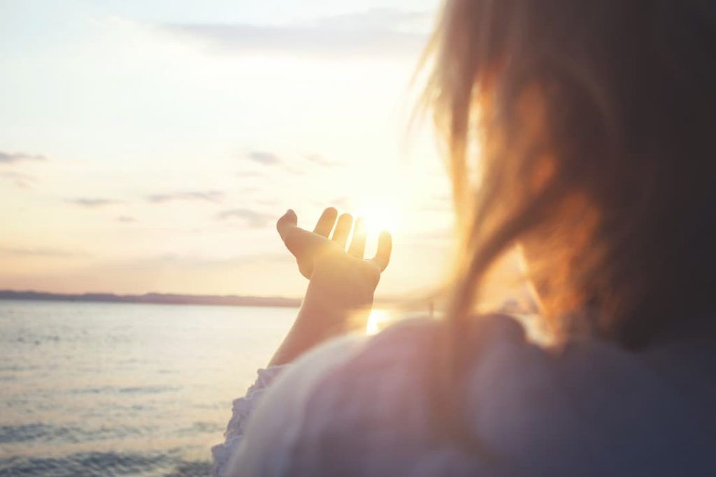 A woman looking at the sunset over the sea and holding her hand out